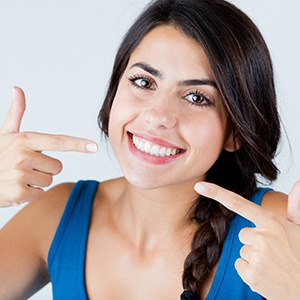 Woman in blue shirt pointing to her smile
