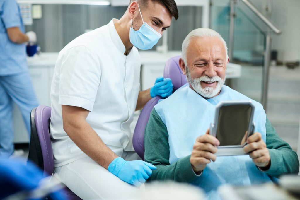 Senior man smiling in mirror at dentist's office