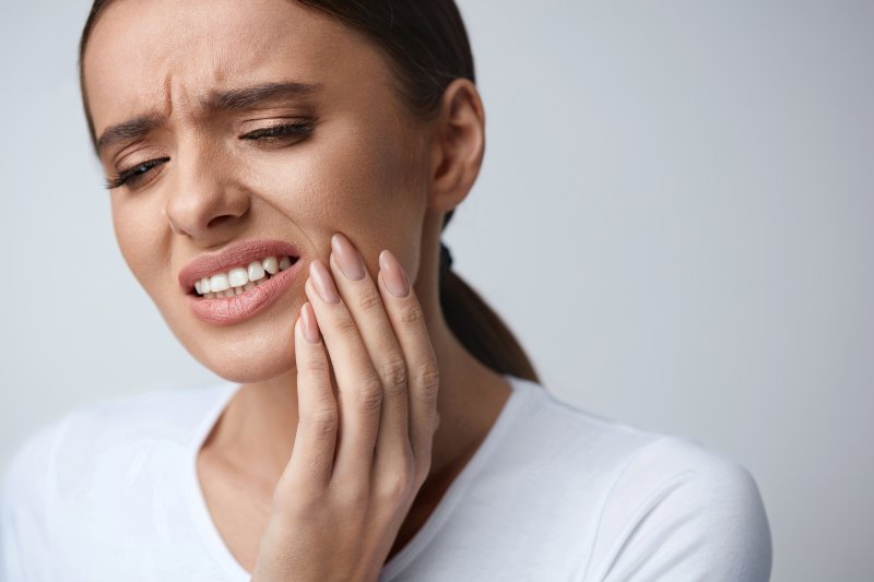 person experiencing tooth pain holding their cheek